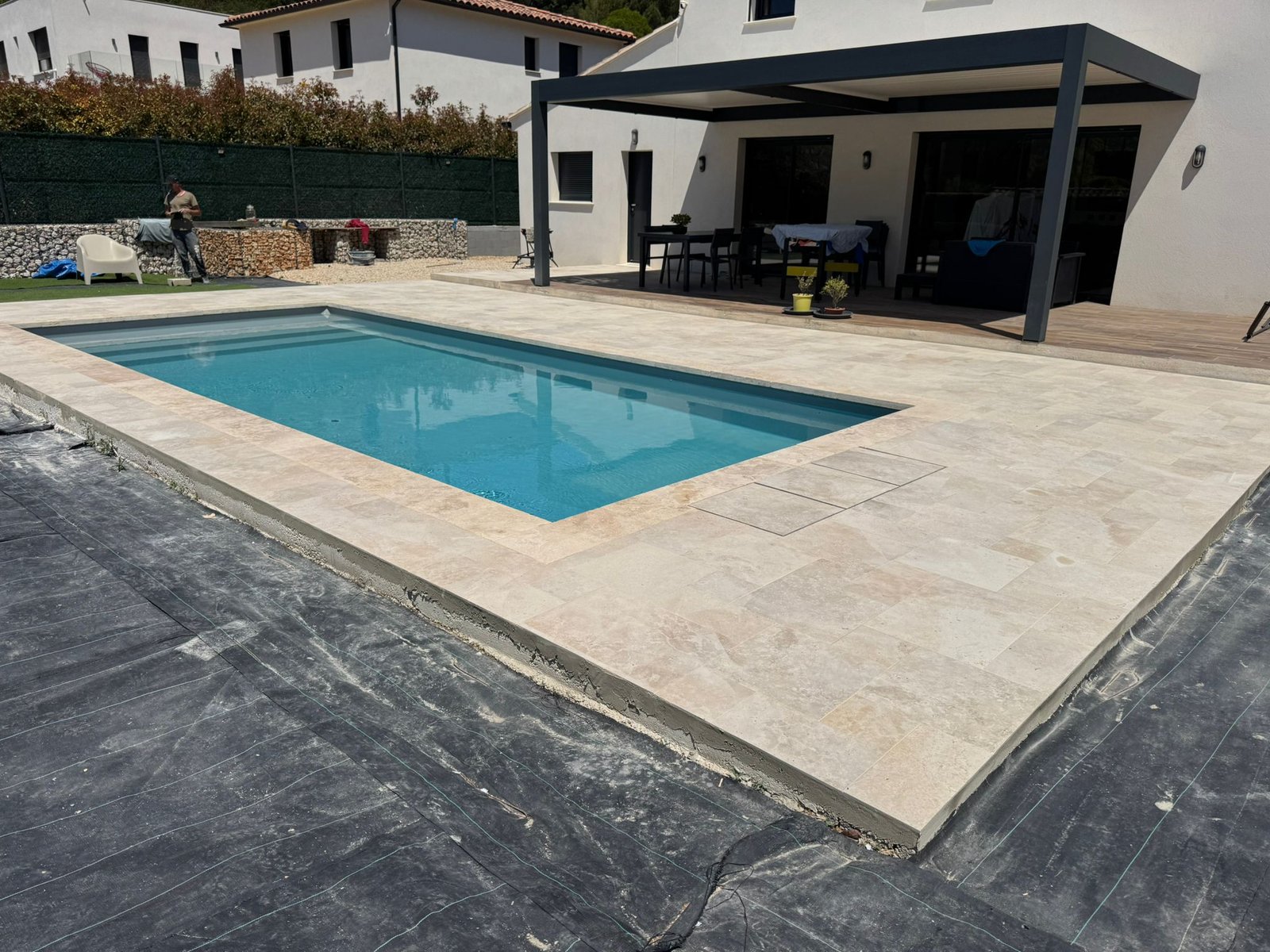 Projet piscine et terrasse - piscine terminée avec eau turquoise, grande terrasse en pierre, pergola moderne