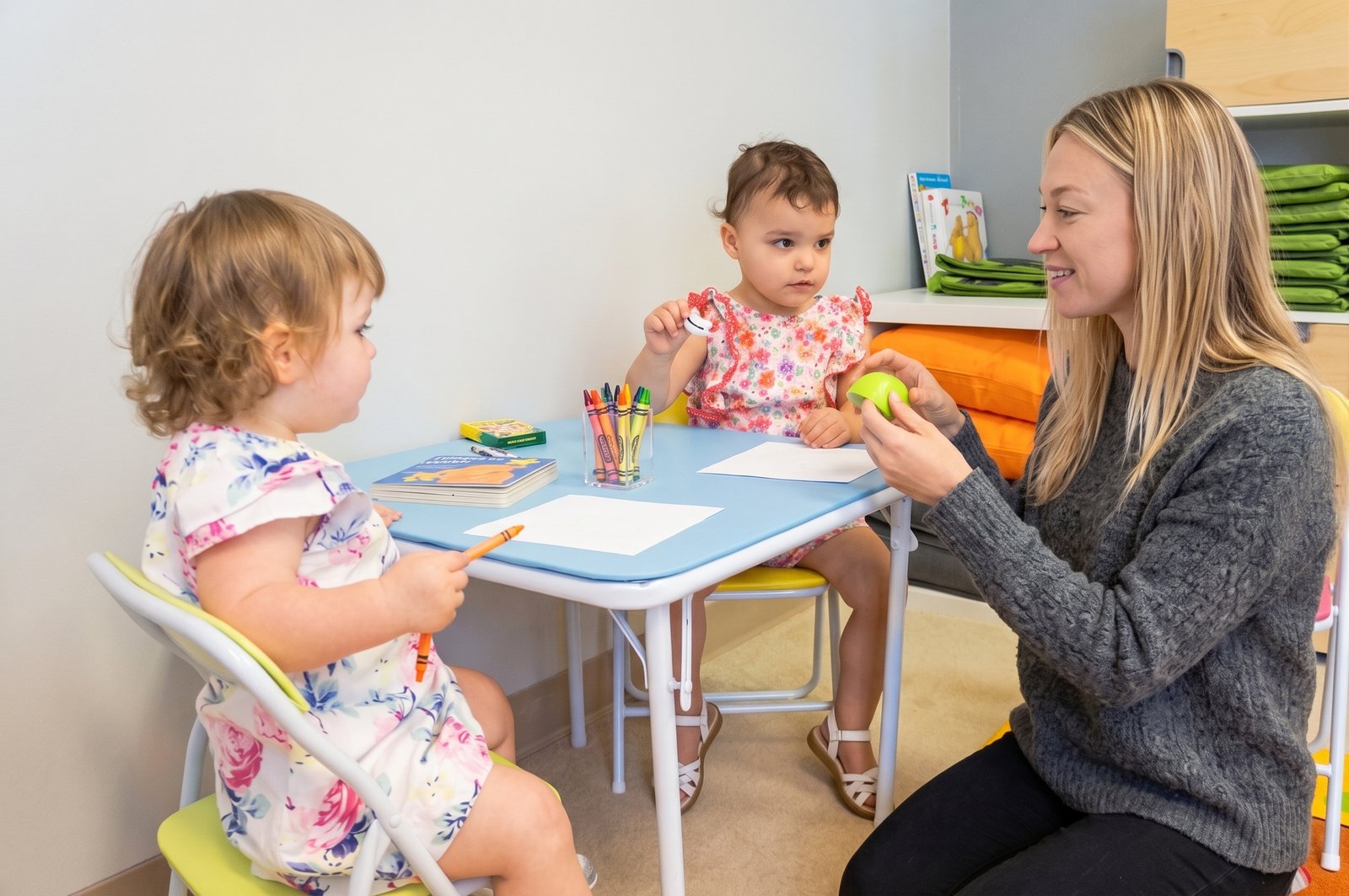 A speech therapist reading a picture book with a preschooler on a playroom rug