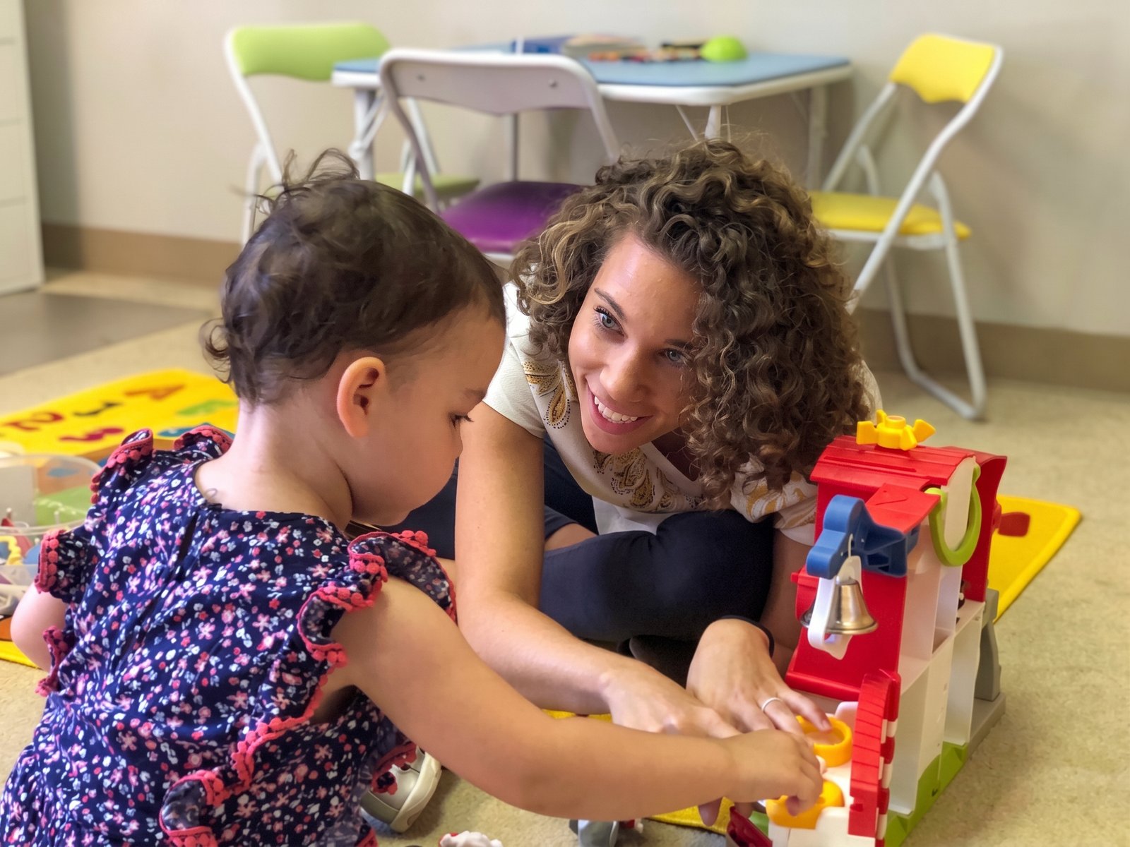 A feeding therapist gently helping a toddler explore colorful foods at a child-sized table
