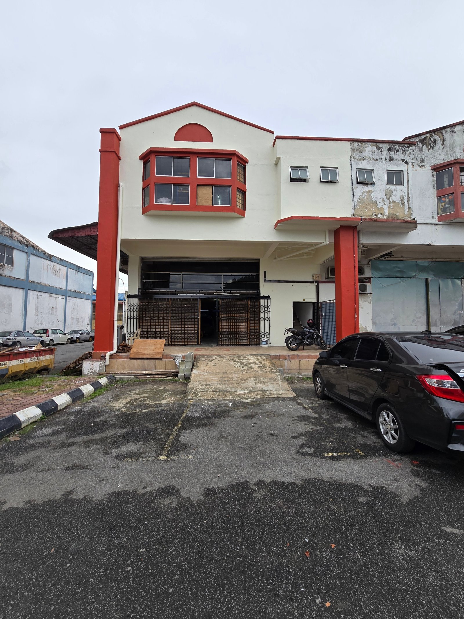 Funzy Global warehouse exterior before renovation with weathered red pillars and peeling white render