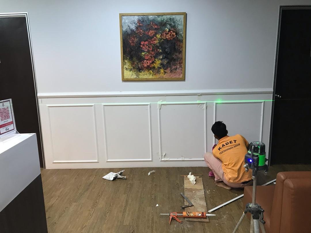 Worker installing white wall panelling at KLEM Clinics with laser level for precision alignment