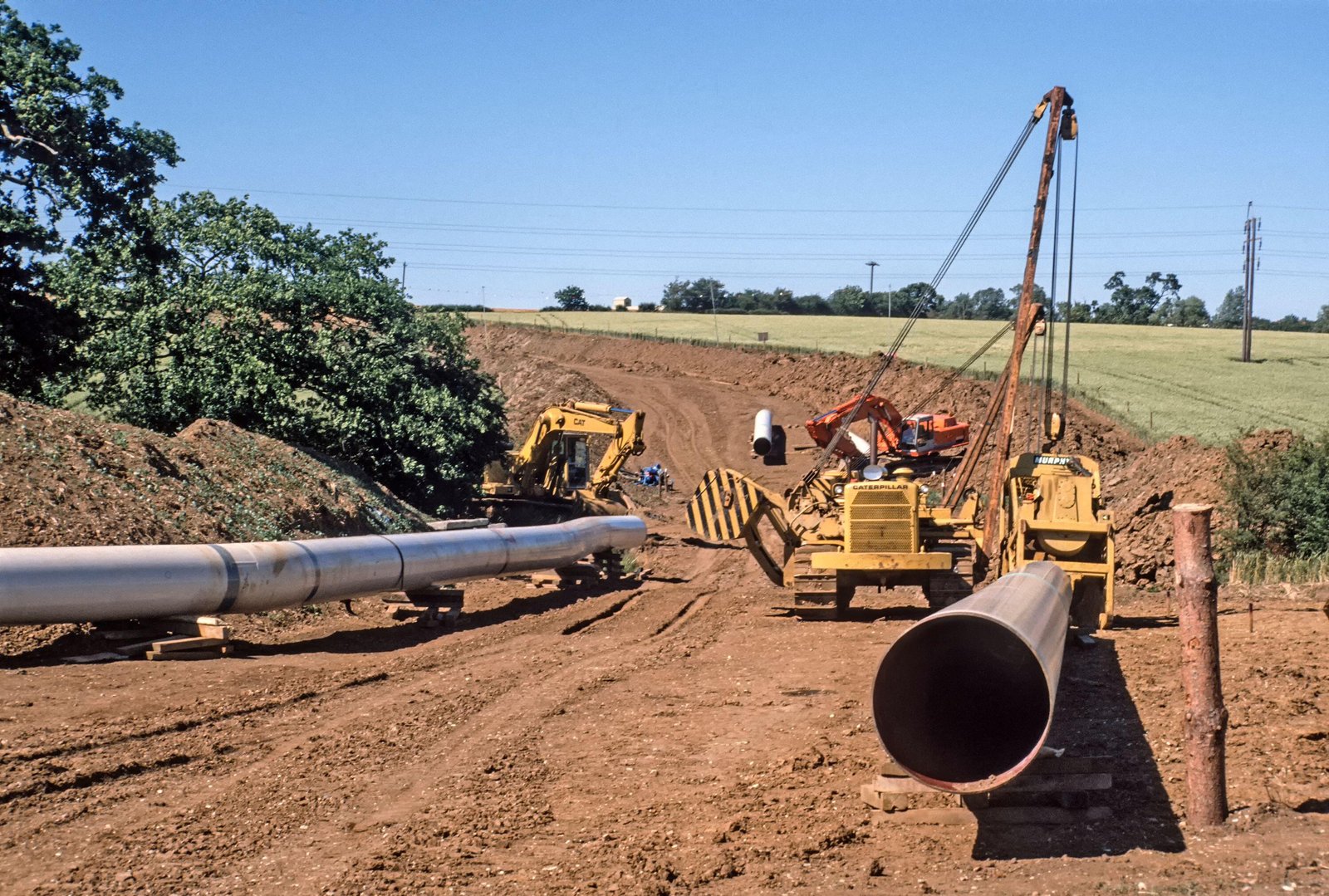 Sideboom pipelayers lowering a steel pipe section into an open trench