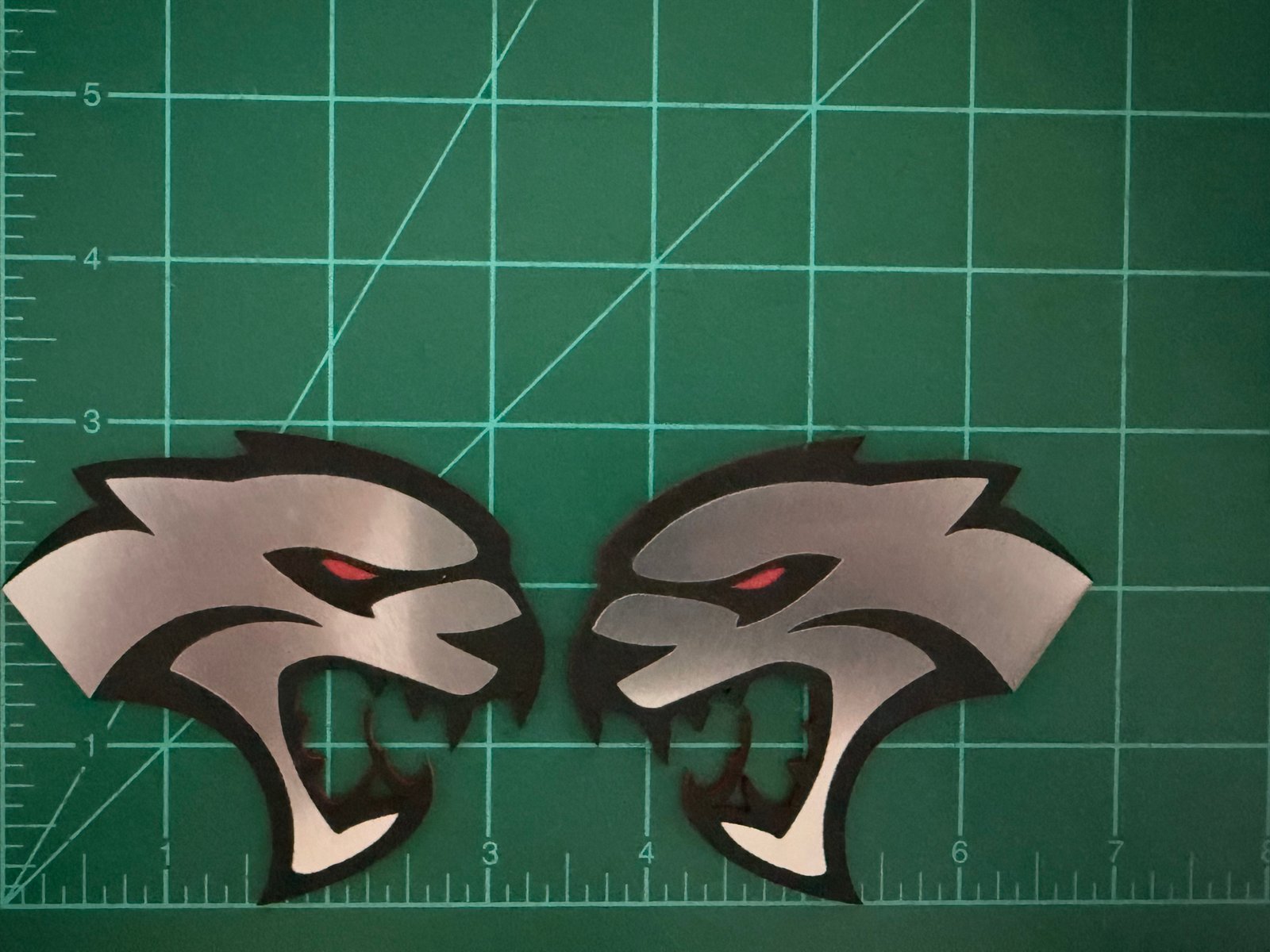 Pair of Hellcat Logo acrylic automotive badges photographed on a green cutting mat