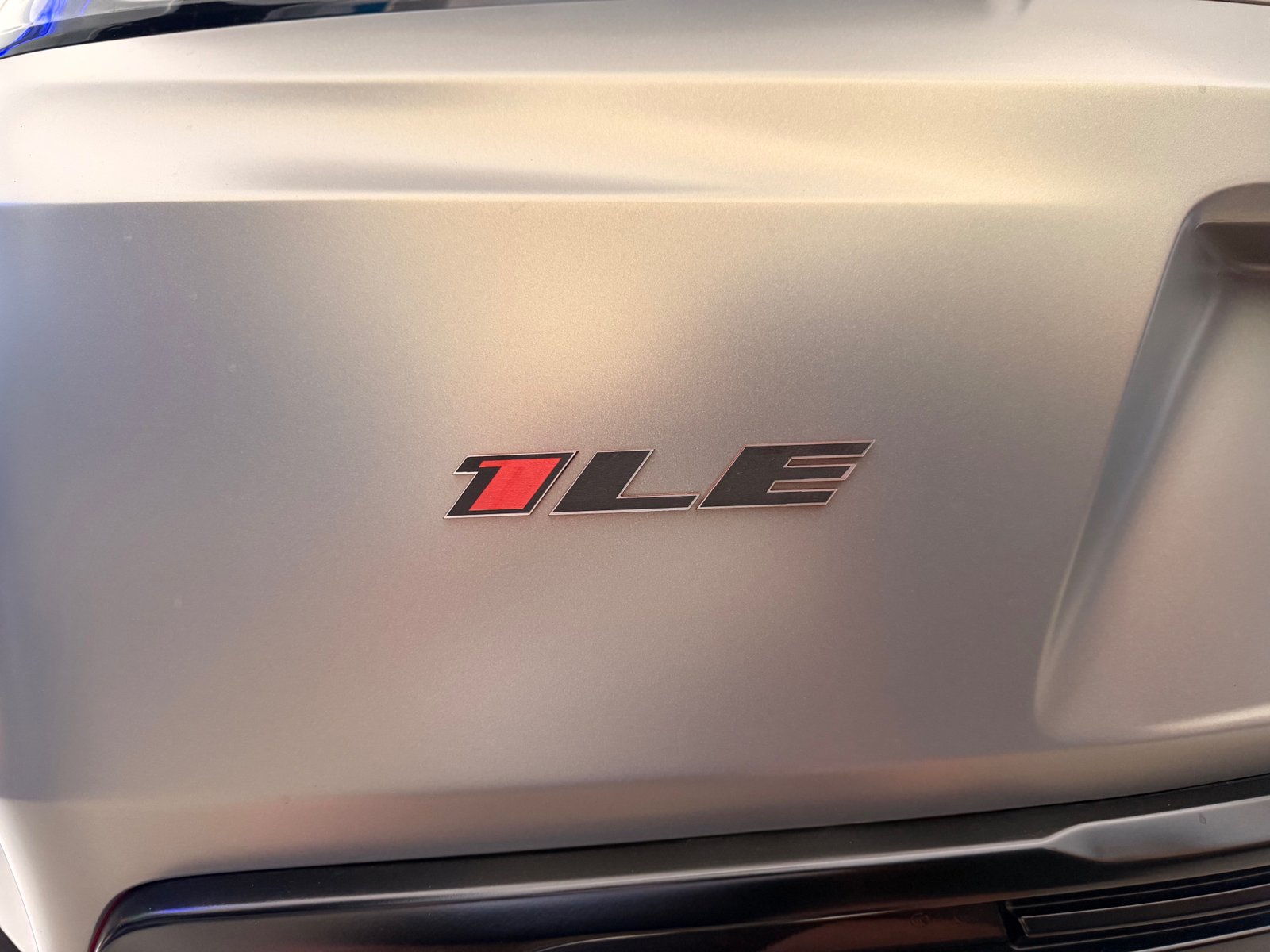 Close-up of a red and black 1LE acrylic automotive badge installed on a silver Camaro trunk