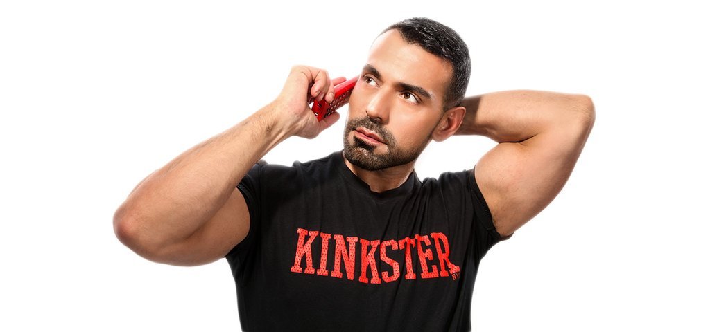 Model in a black Kinkster T-shirt holding a red cap to his ear against a white ground