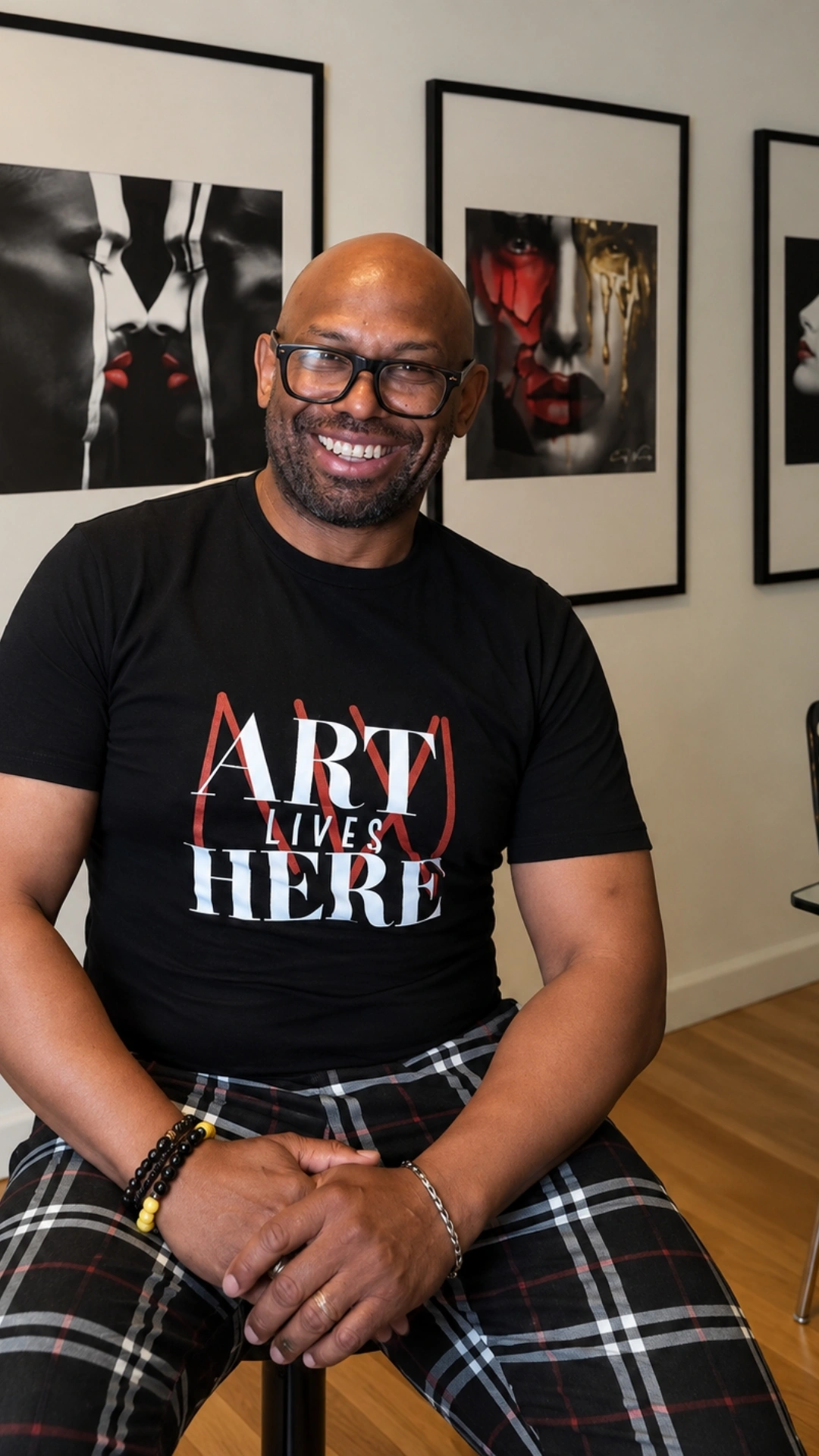 Corey Wesley seated indoors in a black Art Lives Here shirt and plaid pants