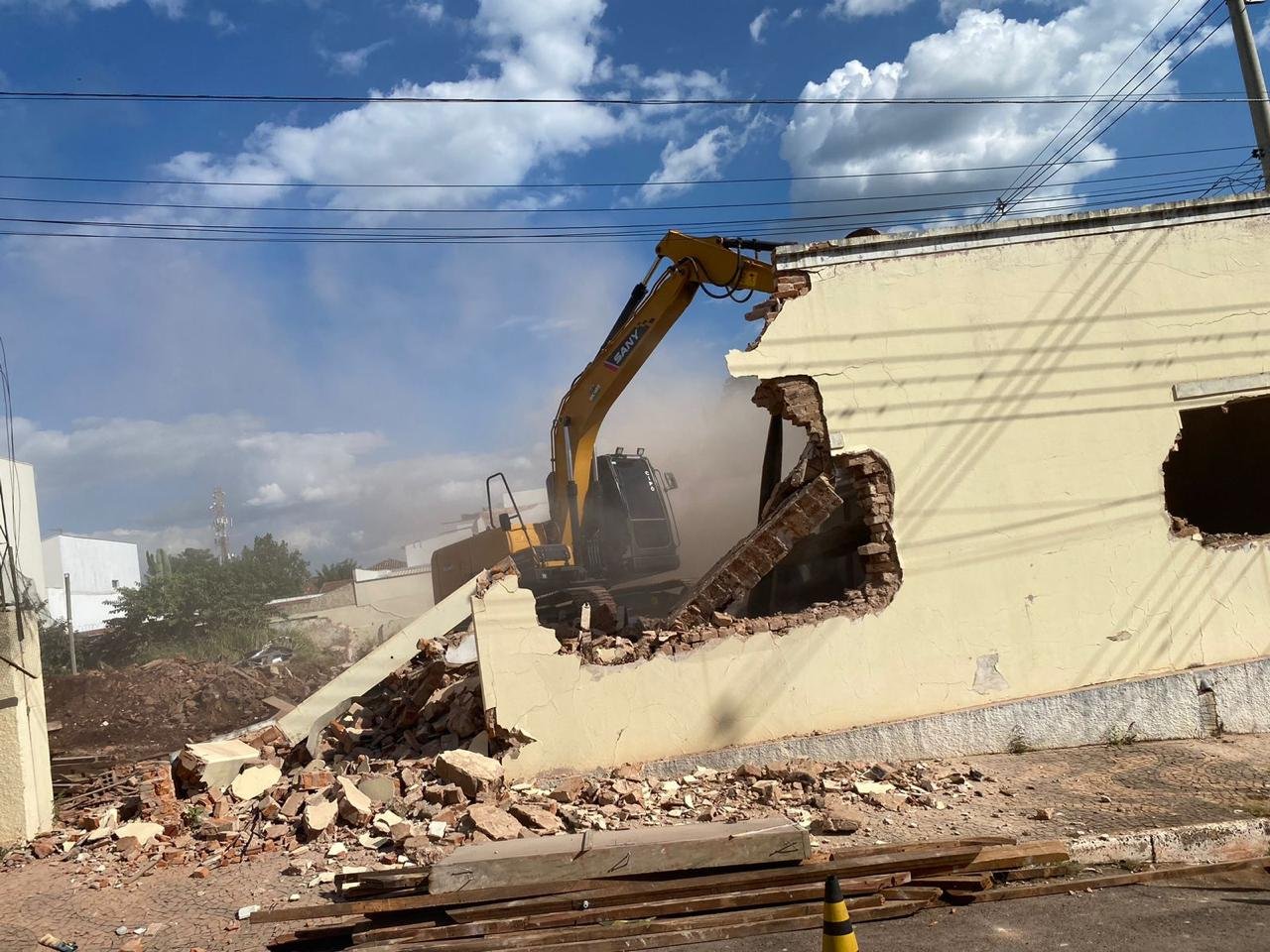 Escavadeira demolindo parede de edificação, com entulho no solo