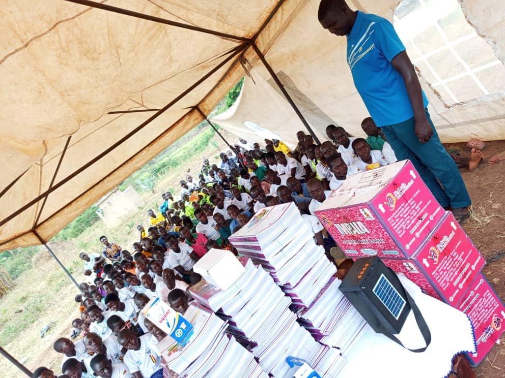 Staff member presenting scholastic materials and textbooks to students at a distribution ceremony