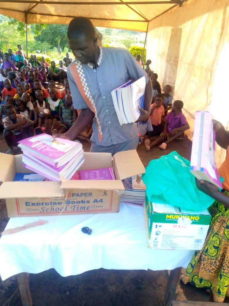 Staff member distributing exercise books and scholastic materials to beneficiaries