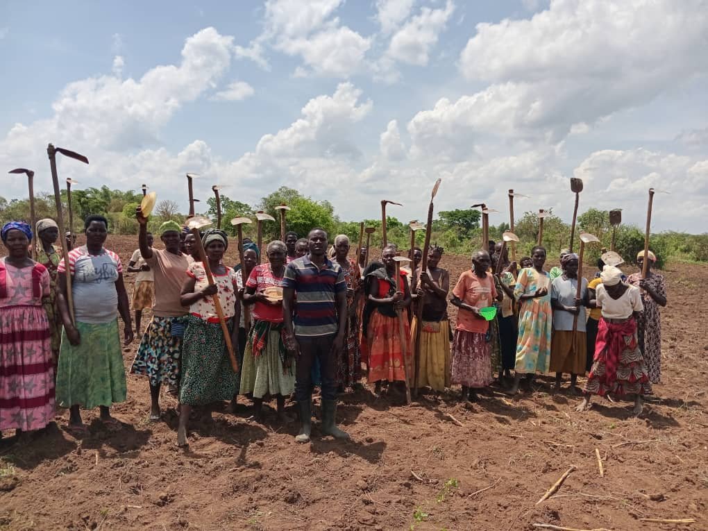 Women holding farm tools at a distribution event in an open field