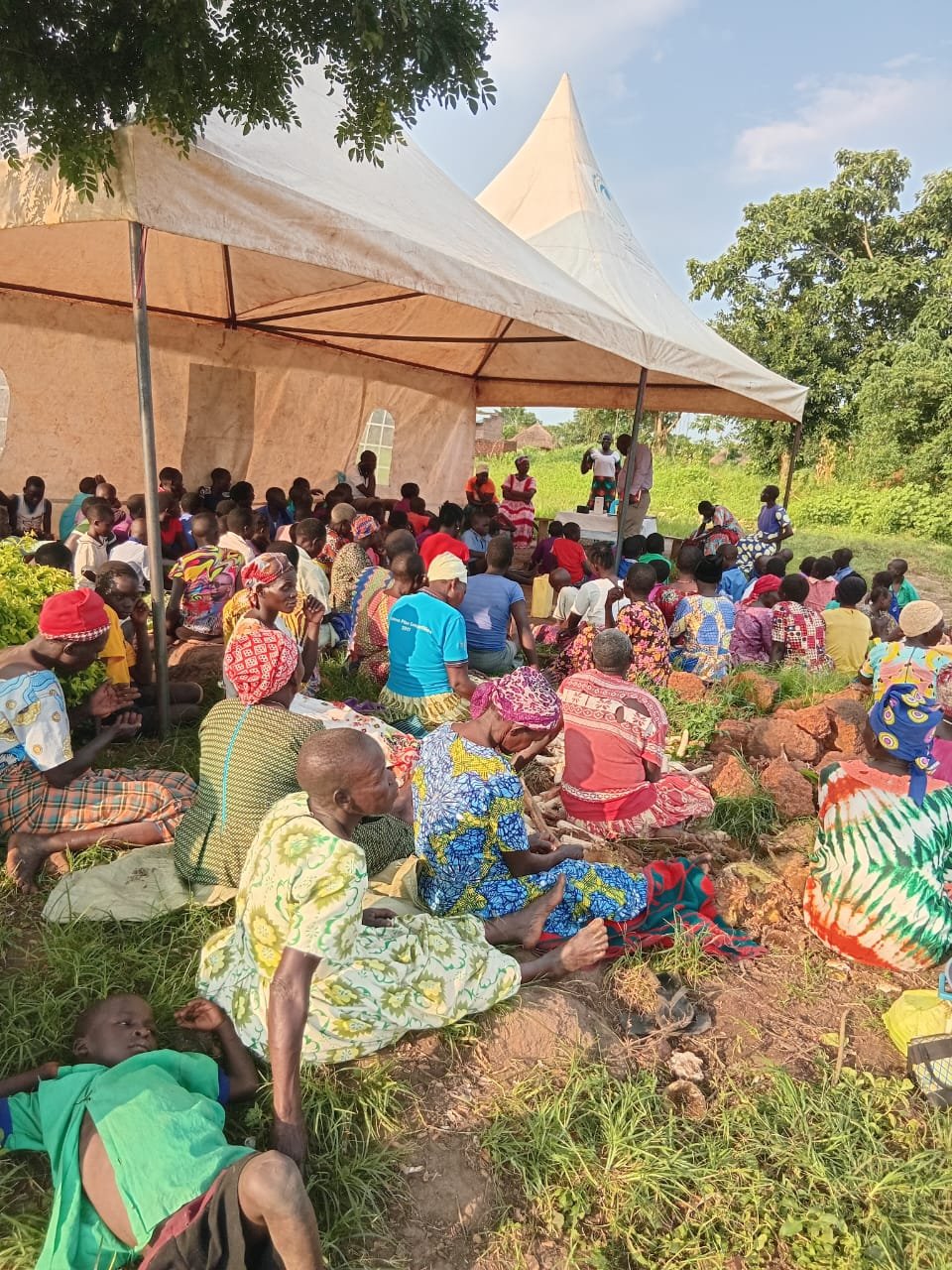 Large community gathering under a tent with multiple attendees at an outdoor event