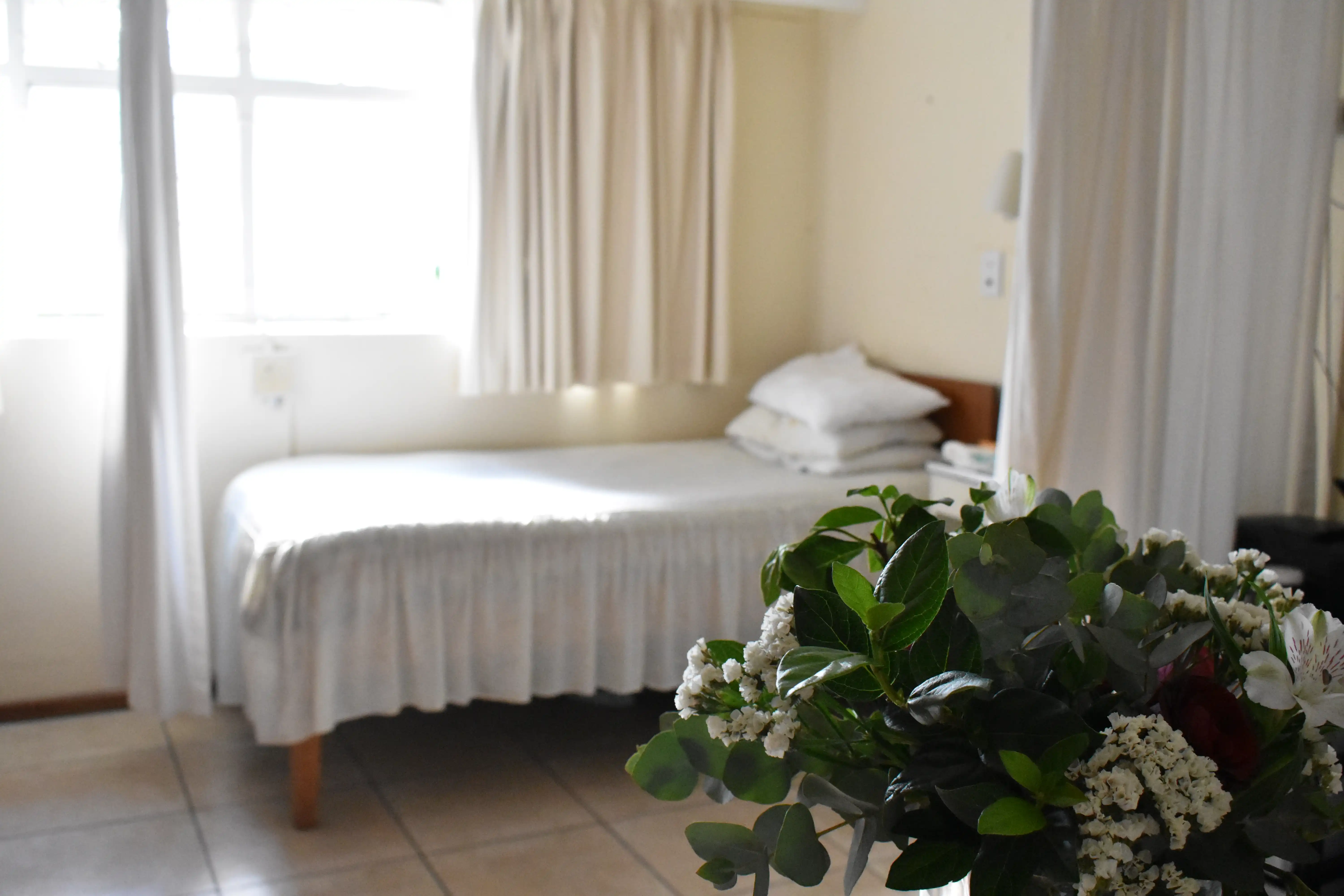 A neatly made bed with fresh flowers in a frail care room at Huis Uitsig