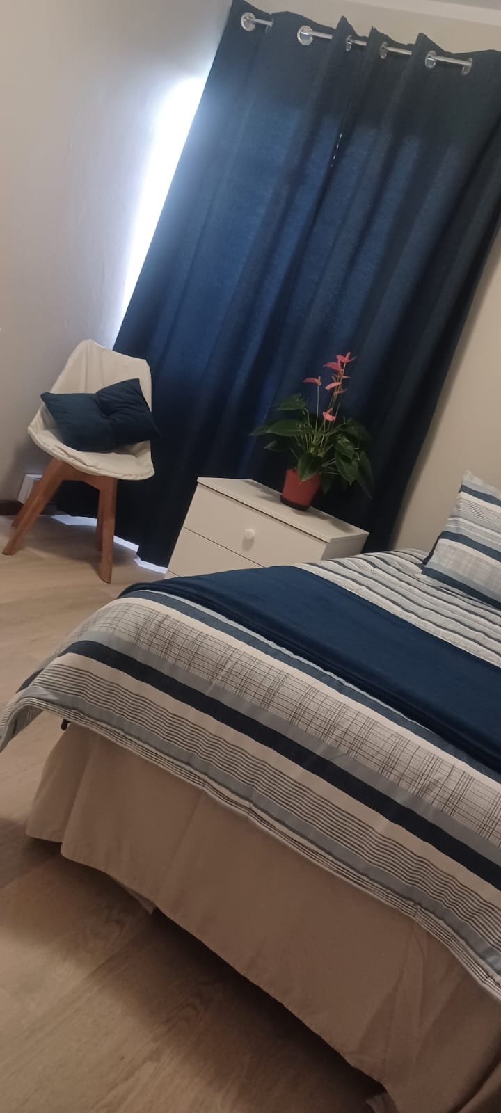A single room with striped bedding, a desk by the window and pink curtains