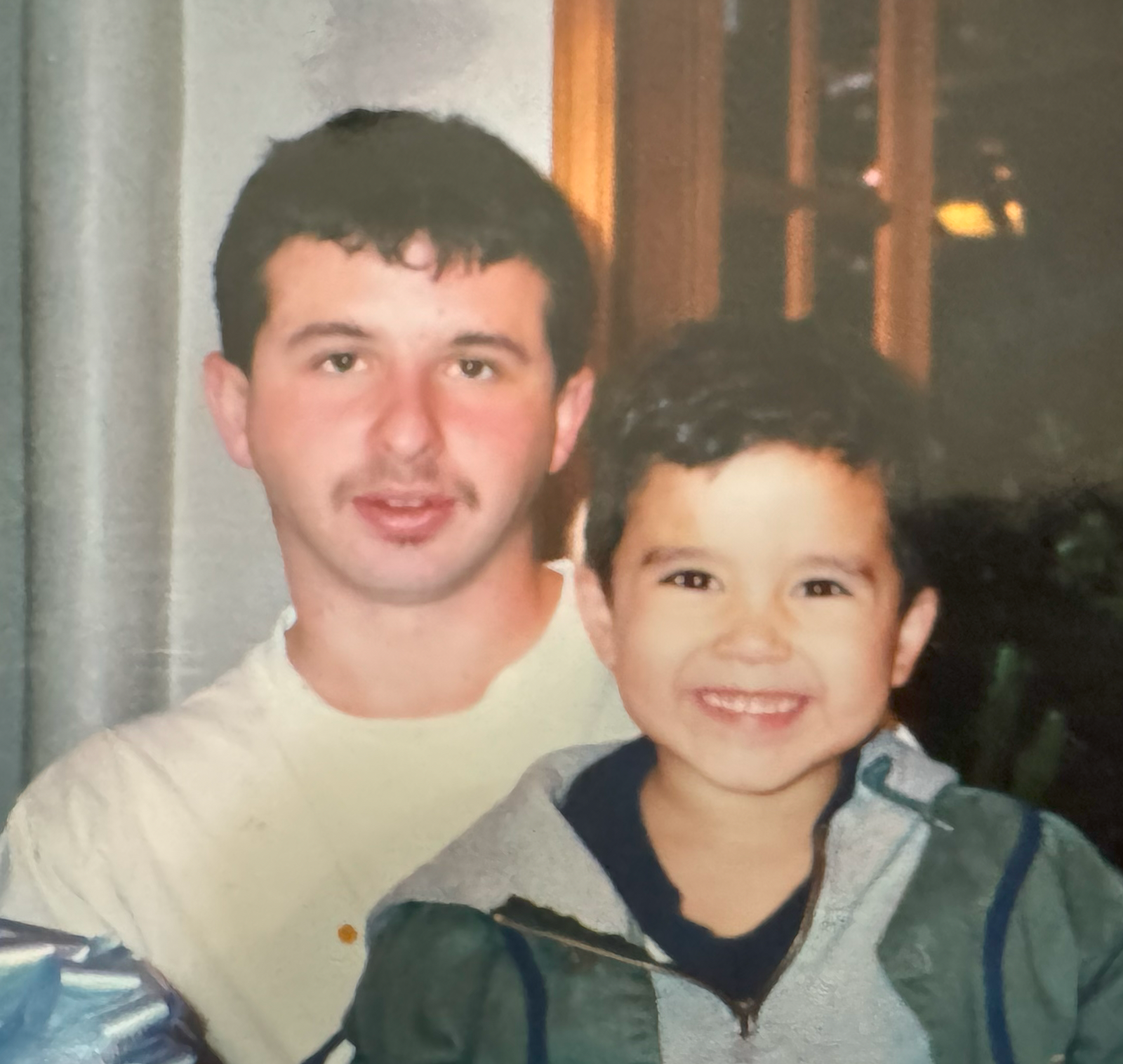 Chris as a young man holding his child, both smiling.