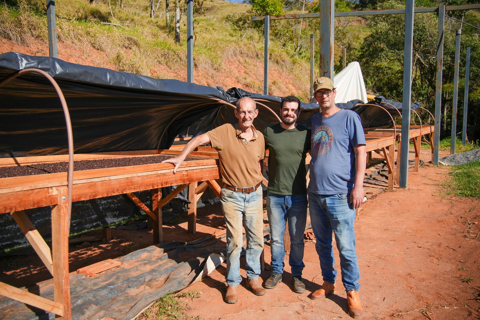 Três homens da equipe diante dos terreiros suspensos na terra vermelha