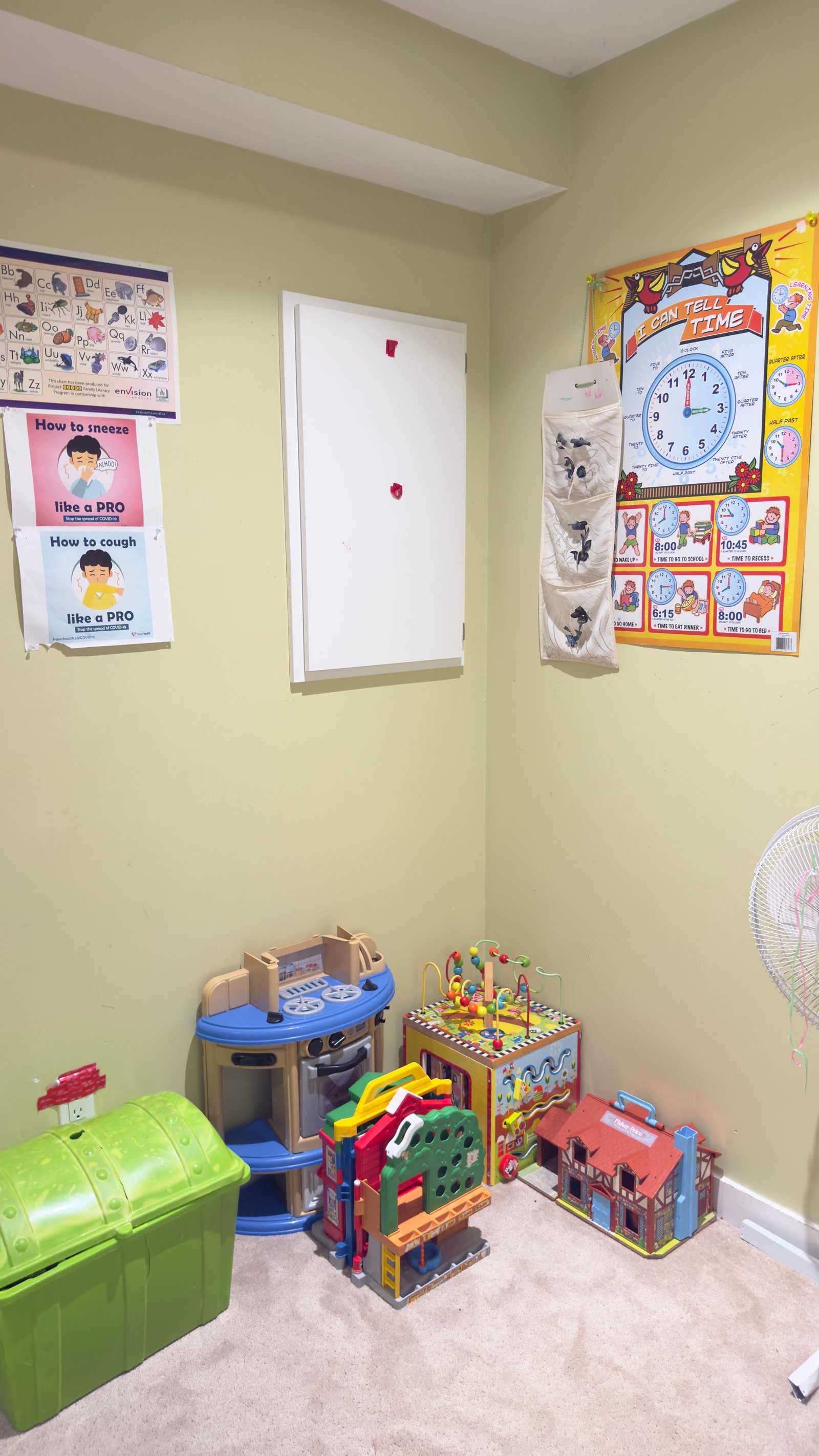Pretend-play corner with toy kitchen, dollhouse, activity cube, and learning posters