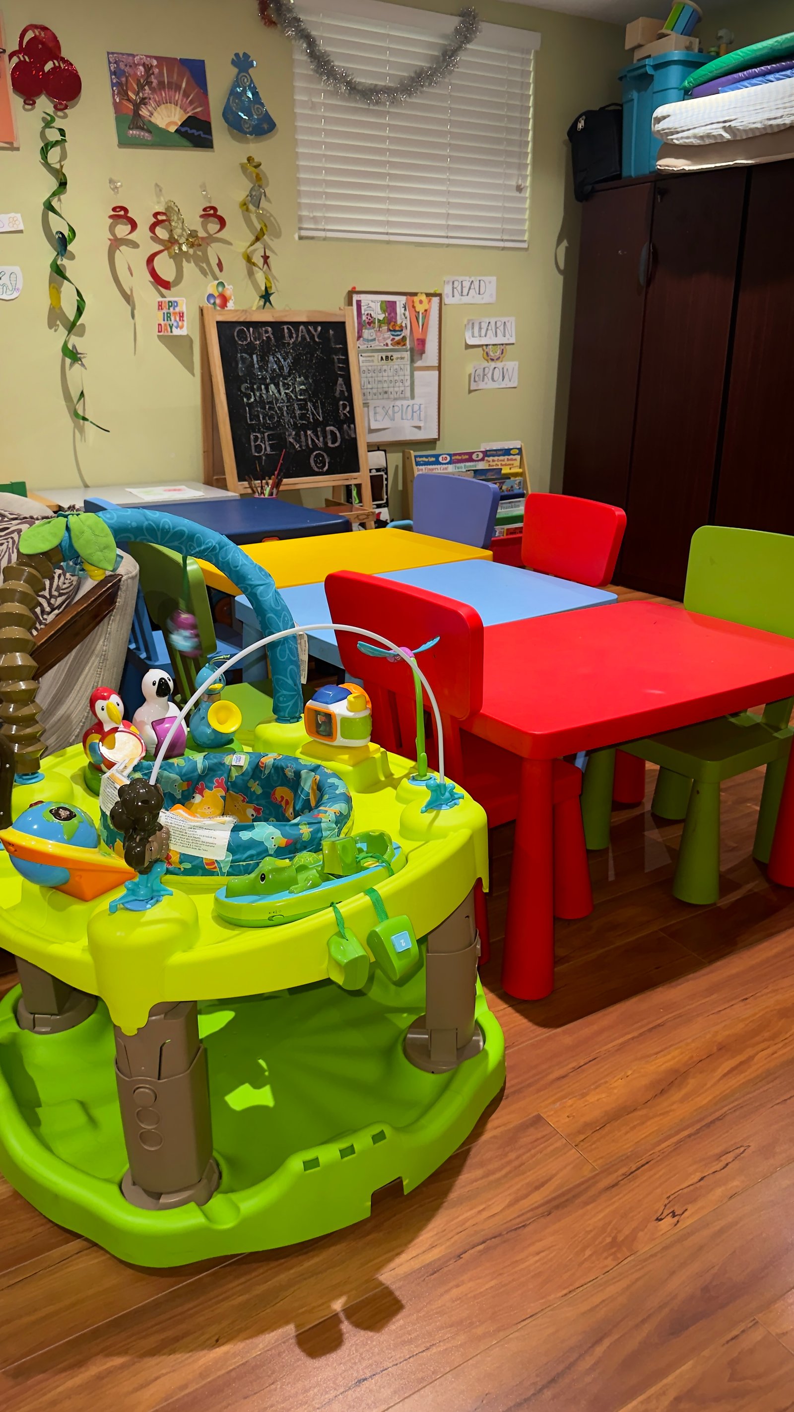 Infant activity centre beside red and green toddler tables in the daycare play space