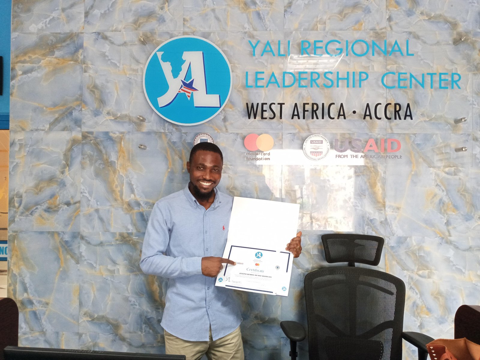 Joe Quarcoo holding a certificate in front of a YALI Regional Leadership Center West Africa backdrop.