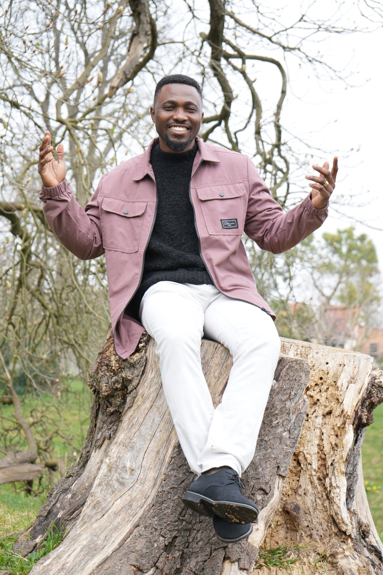 Joe Quarcoo smiling with an open, welcoming gesture outdoors.