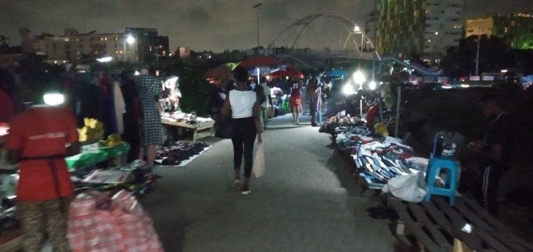 Wide nighttime view of street vendors and customers in the Accra Mall Enclave.