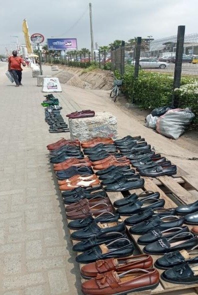 Rows of footwear arranged for sale along a pedestrian route in the Accra Mall Enclave.