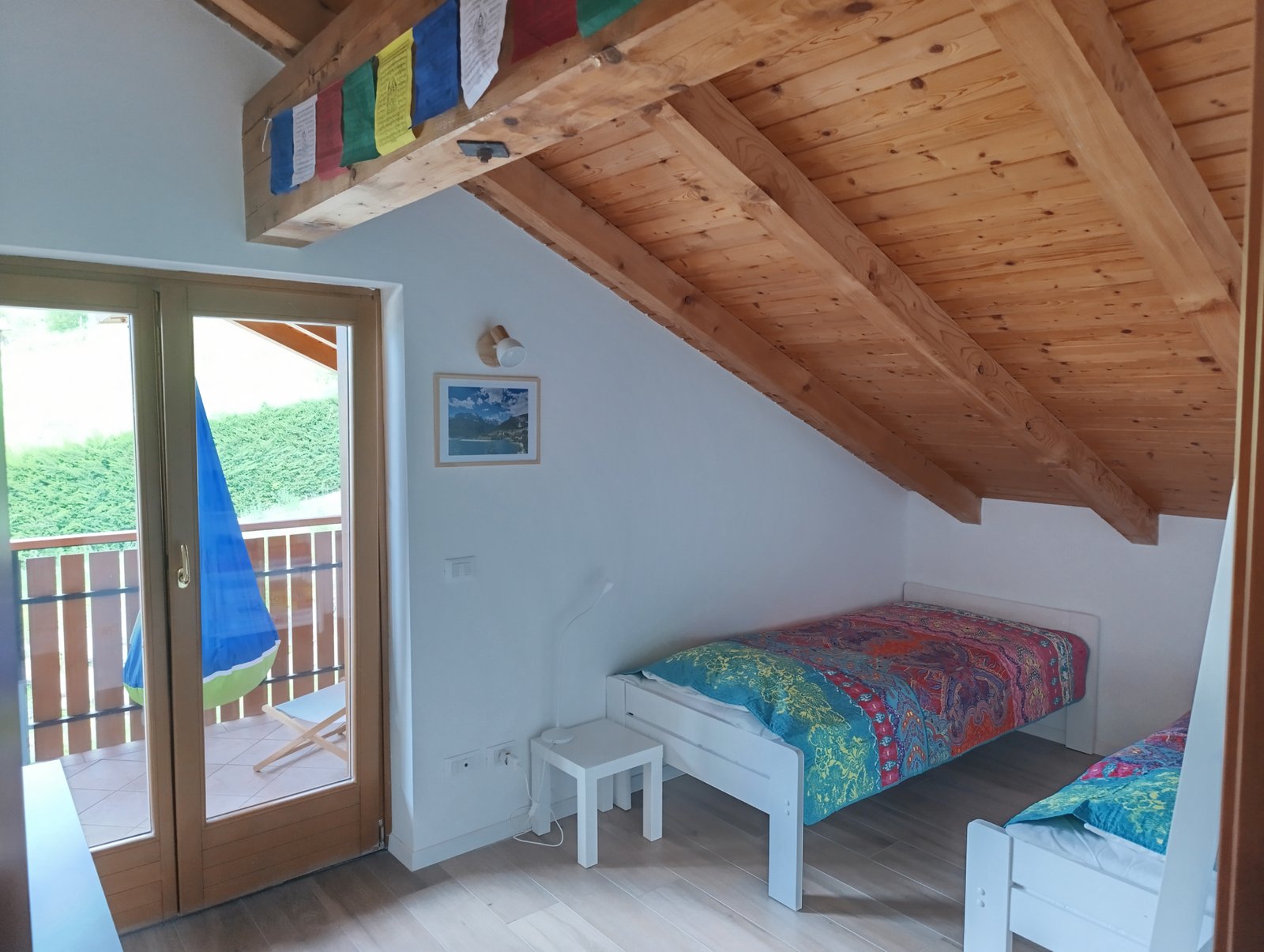 Attic bedroom with wooden ceiling beams, twin beds with colorful quilts and balcony door