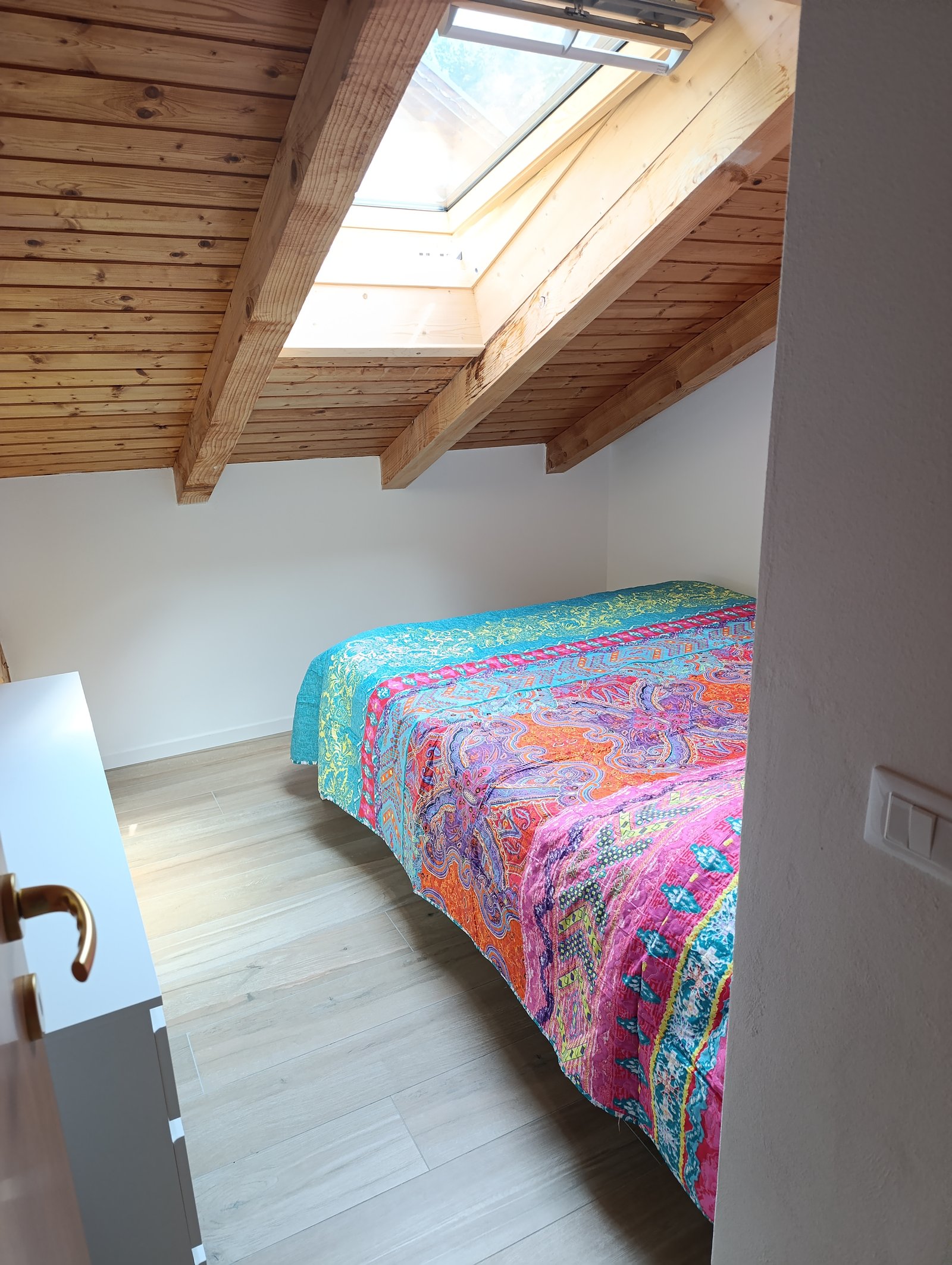 Bright bedroom with colorful bedspread, wooden ceiling beams and skylight windows