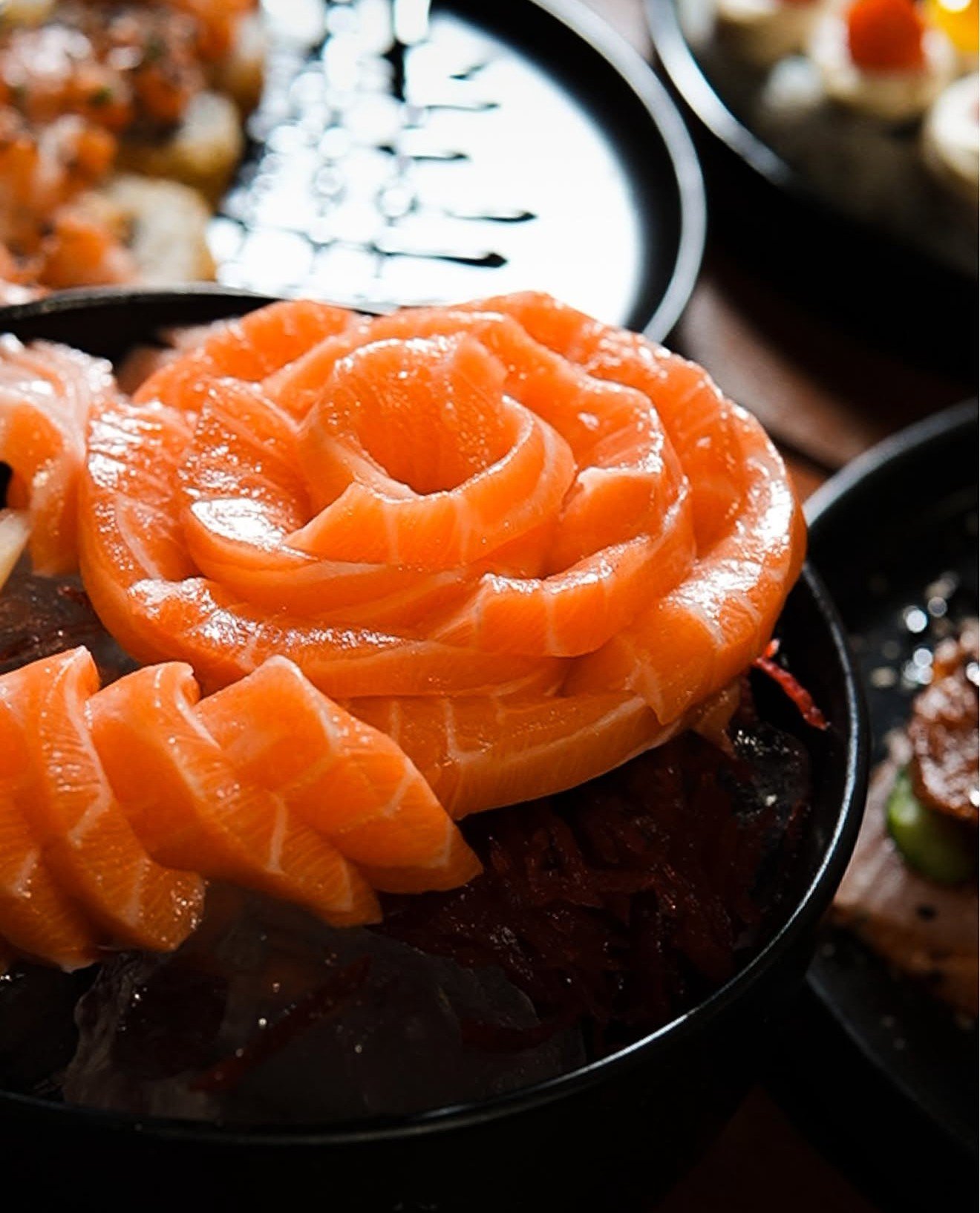 Rosa de sashimi de salmão montada sobre prato preto