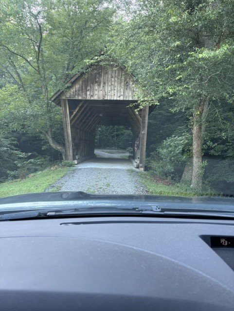 Covered bridge or carport entrance view with gravel driveway