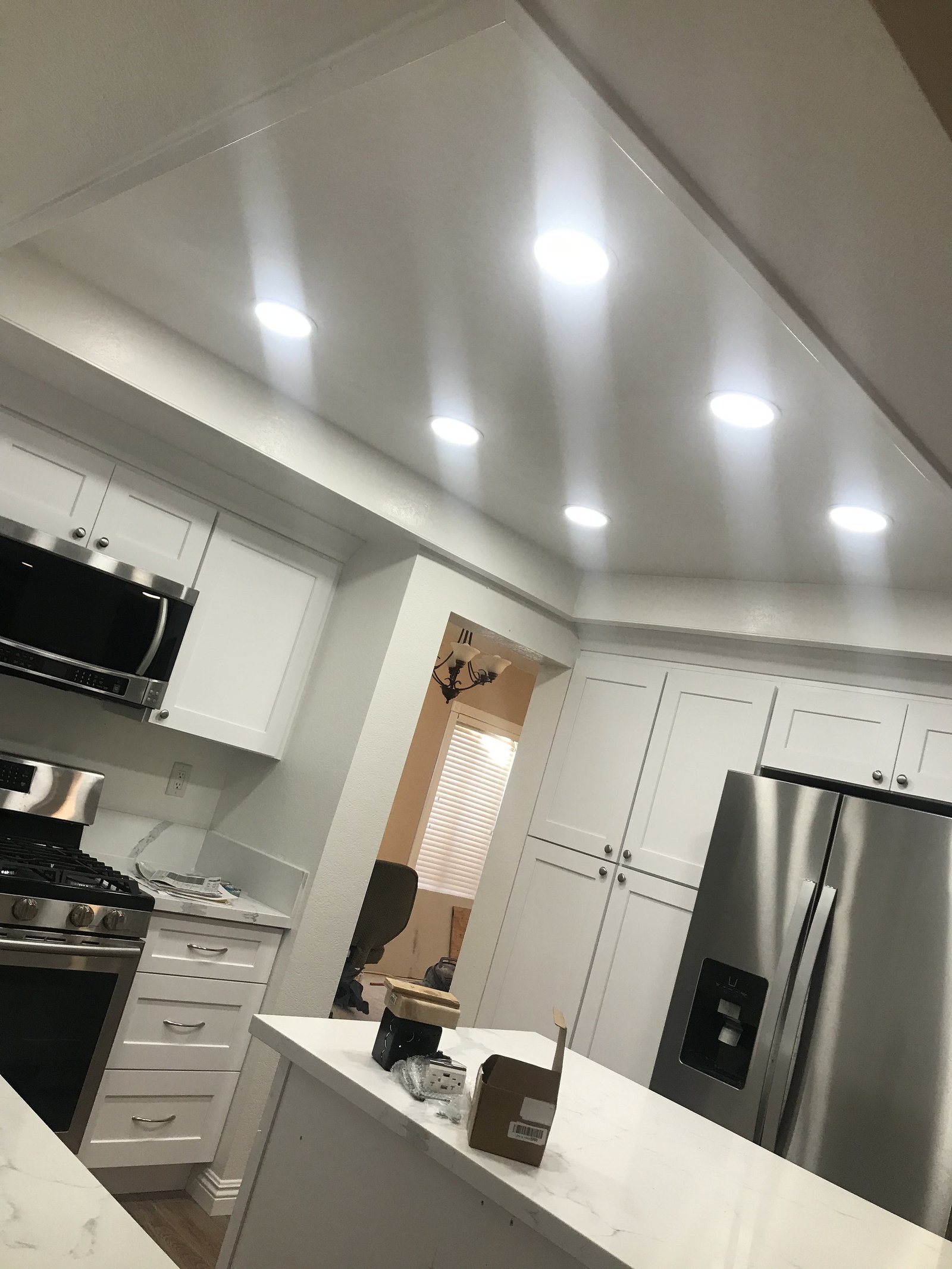After: finished white kitchen ceiling with recessed LED lighting, white cabinets, and stainless appliances