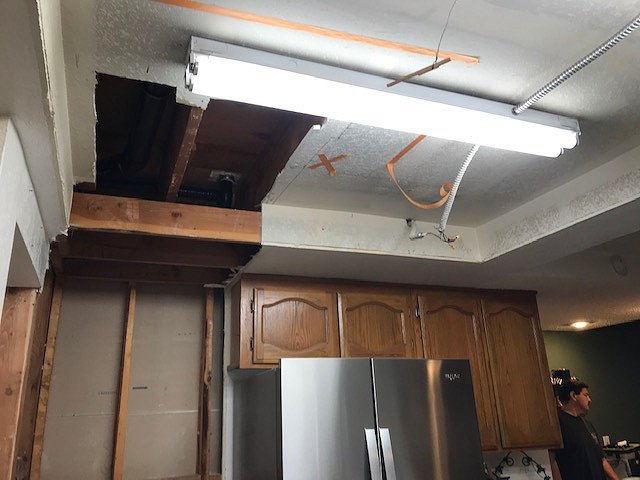Before: damaged kitchen ceiling with open framing and temporary fluorescent light fixture