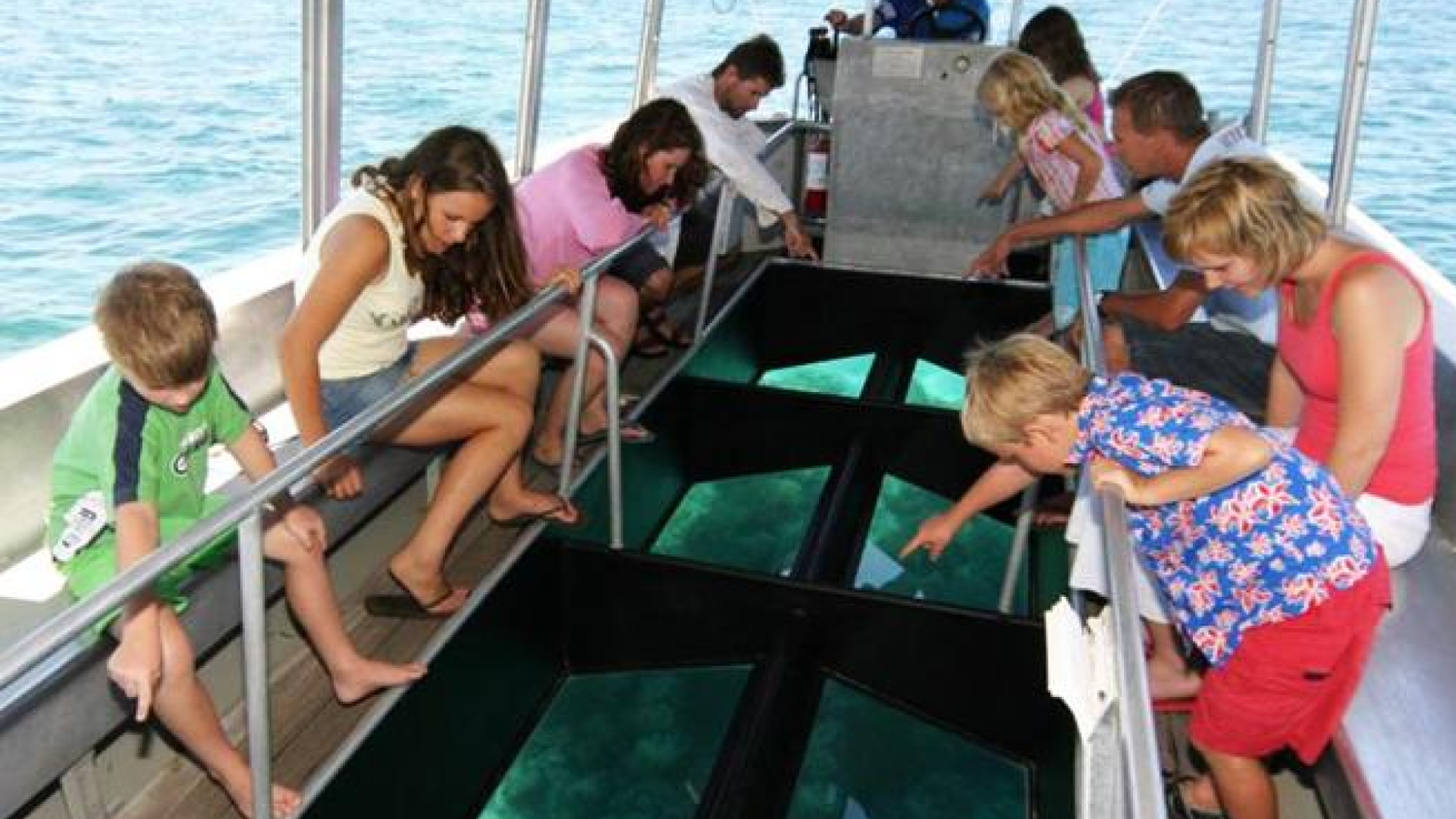 Children and adults looking down through the glass-bottom boat floor into turquoise water at Tanjung Benoa