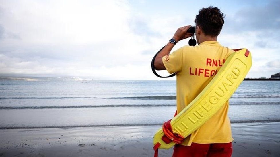 Sauveteur français en surveillance sur une plage, en t-shirt jaune et short rouge, face à l’océan