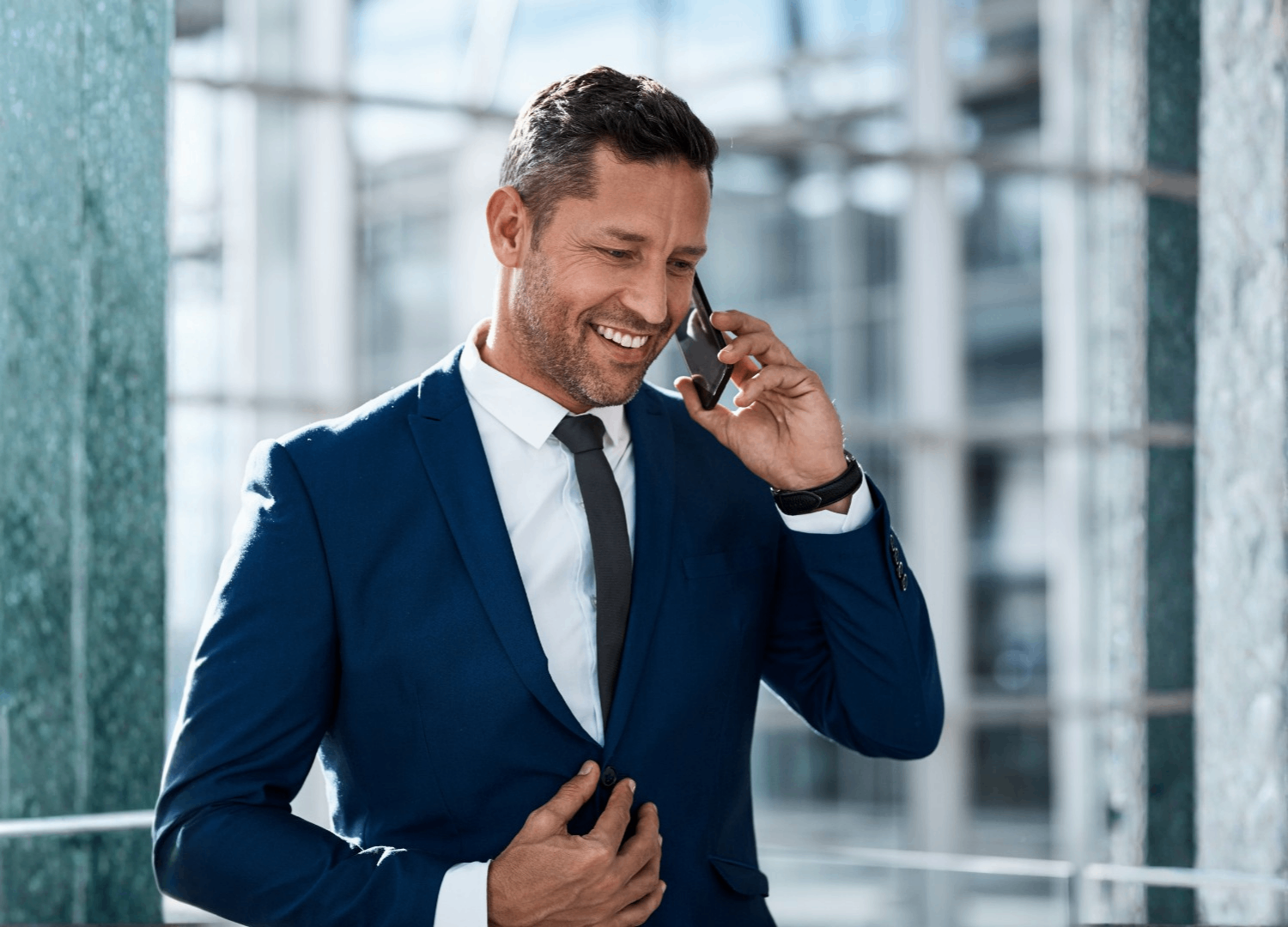 Professional man in blue suit on phone in modern office with city buildings in background