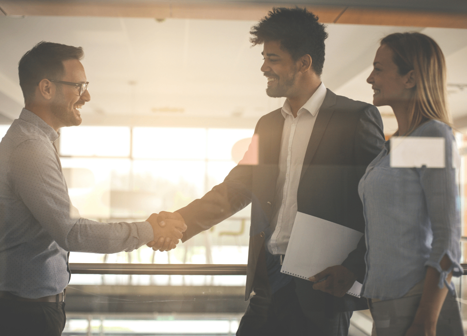 Three professionals shaking hands in a modern office with warm lighting