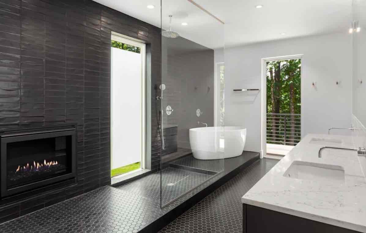 Luxury spa bathroom with dark tile fireplace, freestanding white soaking tub, glass shower, and outdoor patio access