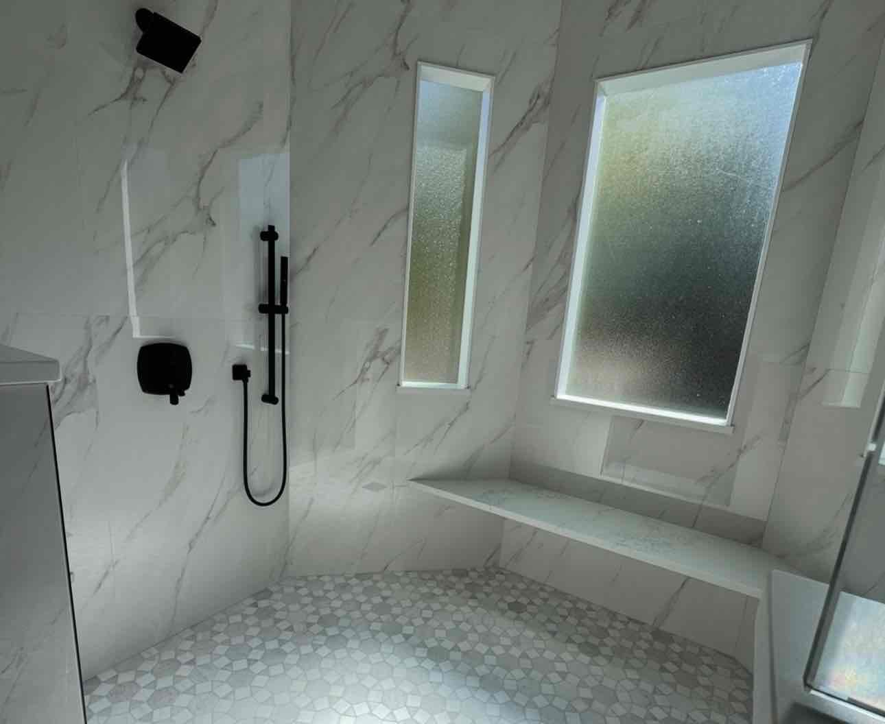 Modern marble bathroom with black fixtures, built-in bench, and frosted glass windows