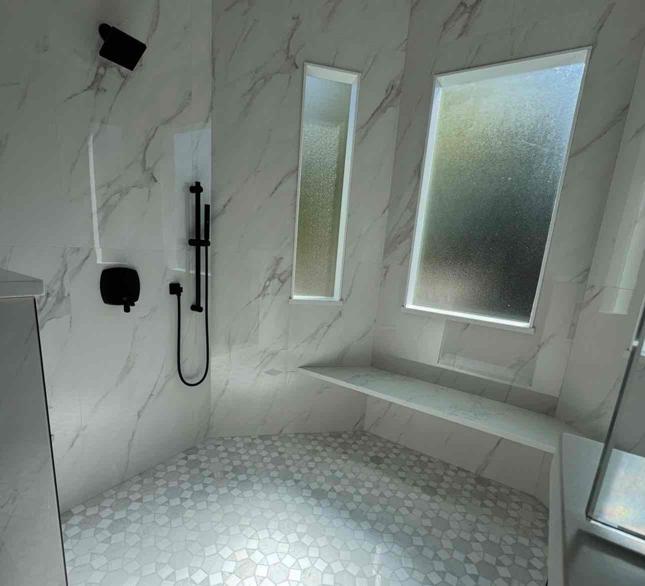 Modern marble bathroom with black fixtures, built-in bench, and frosted glass windows