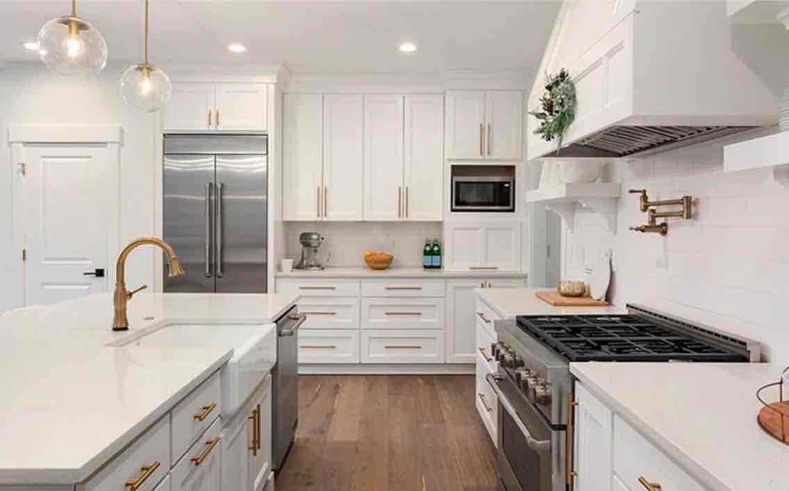 Modern white kitchen with stainless steel appliances, white cabinetry, brass pendant lights, and wood flooring