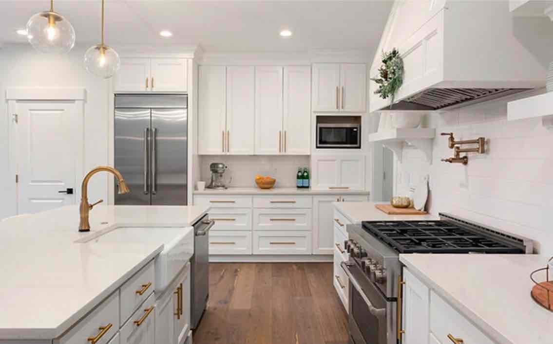 Modern white kitchen with stainless steel appliances, white cabinetry, brass pendant lights, and wood flooring in Chevy Chase home
