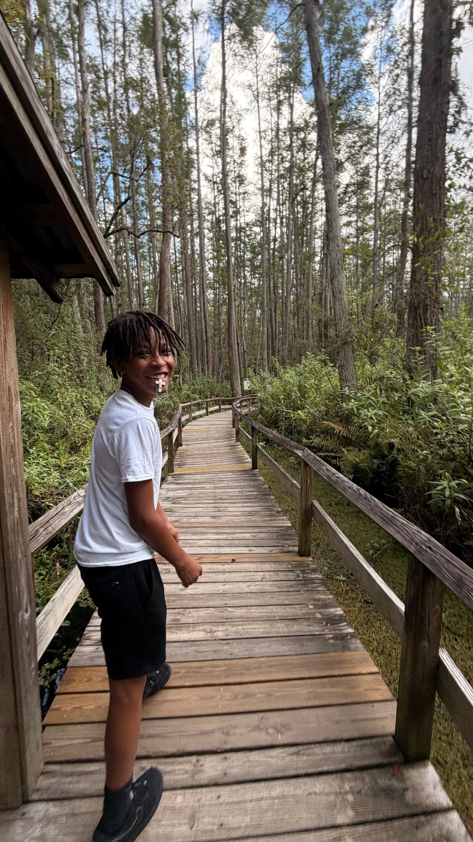 A child walking along a wooden boardwalk through a forest