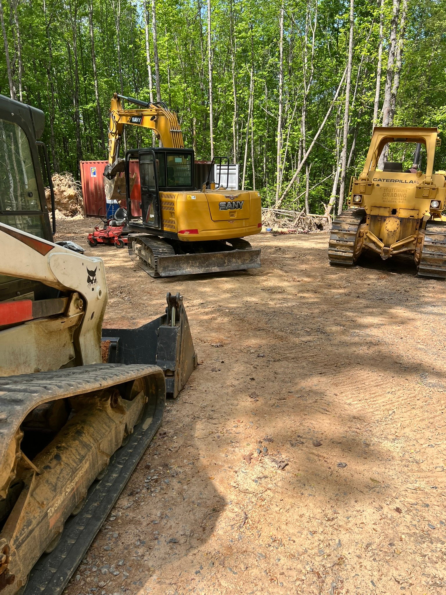 Multiple pieces of heavy equipment in yard - excavators, skid steers, and other machinery