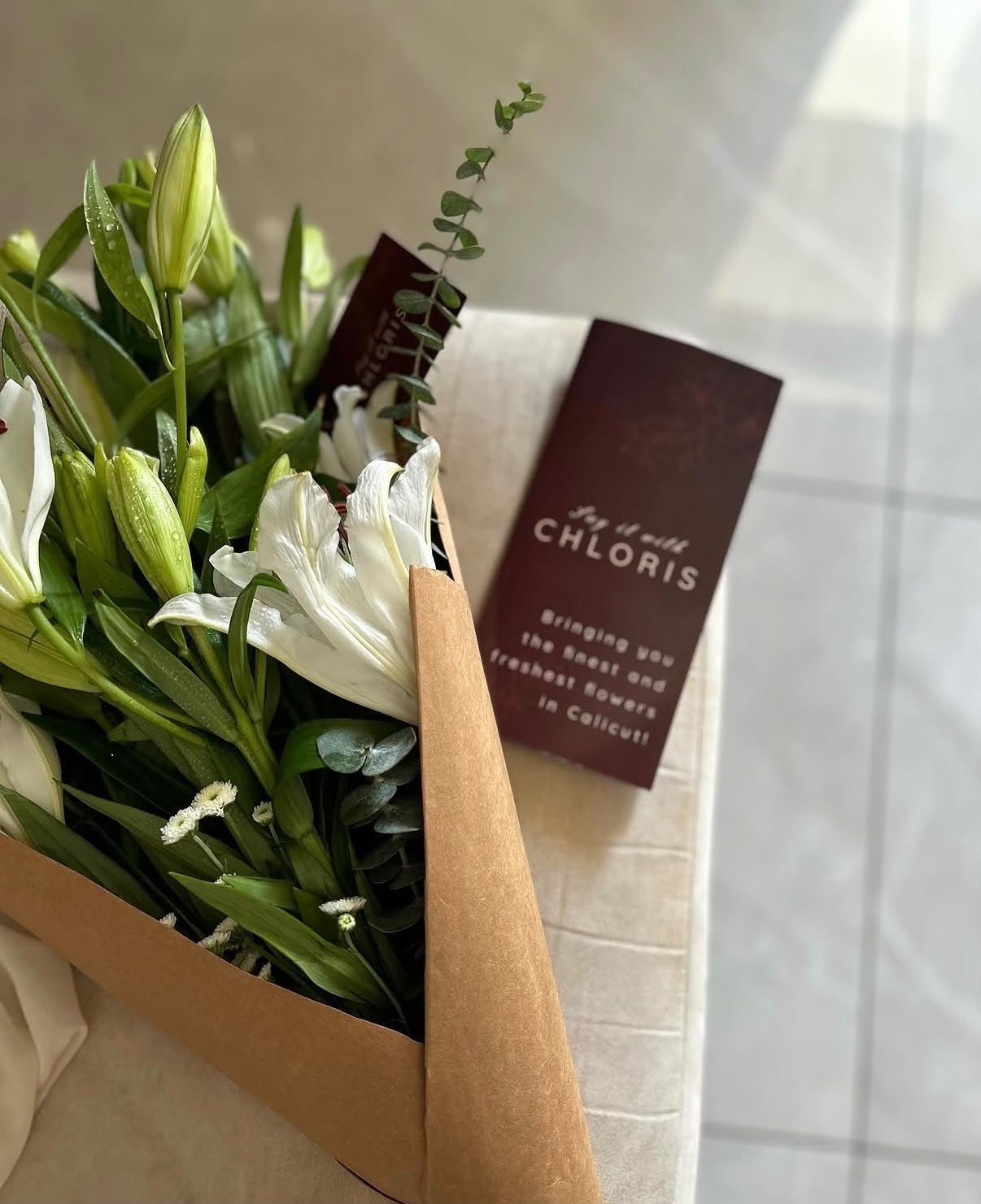 Fresh white lilies from CHLORIS with a brand card reading Bringing you the finest and freshest flowers in Calicut