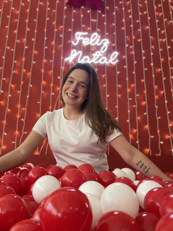 Visitante na piscina de bolinhas vermelhas e brancas, sob o neon Feliz Natal