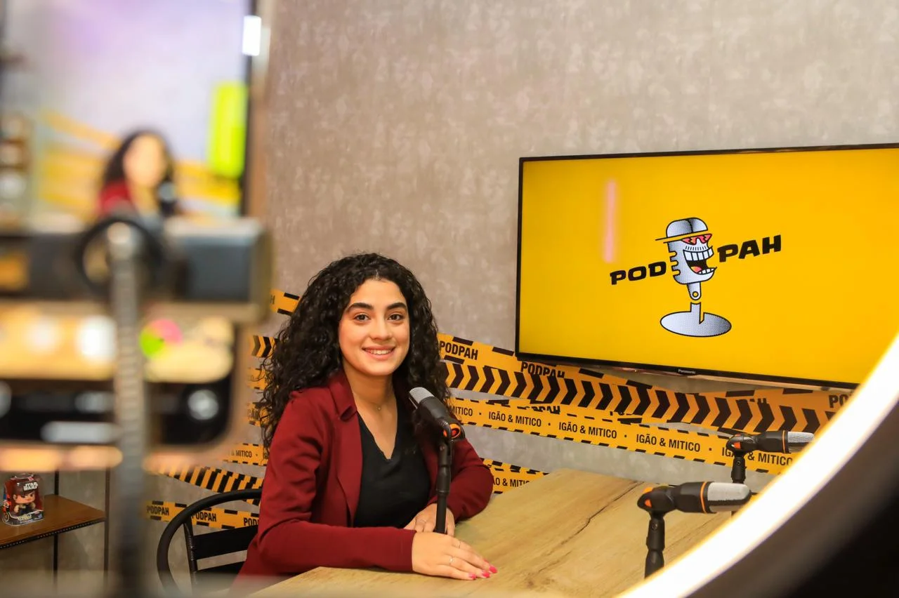 Visitante no estúdio de podcast, com microfones e tela amarela ao fundo