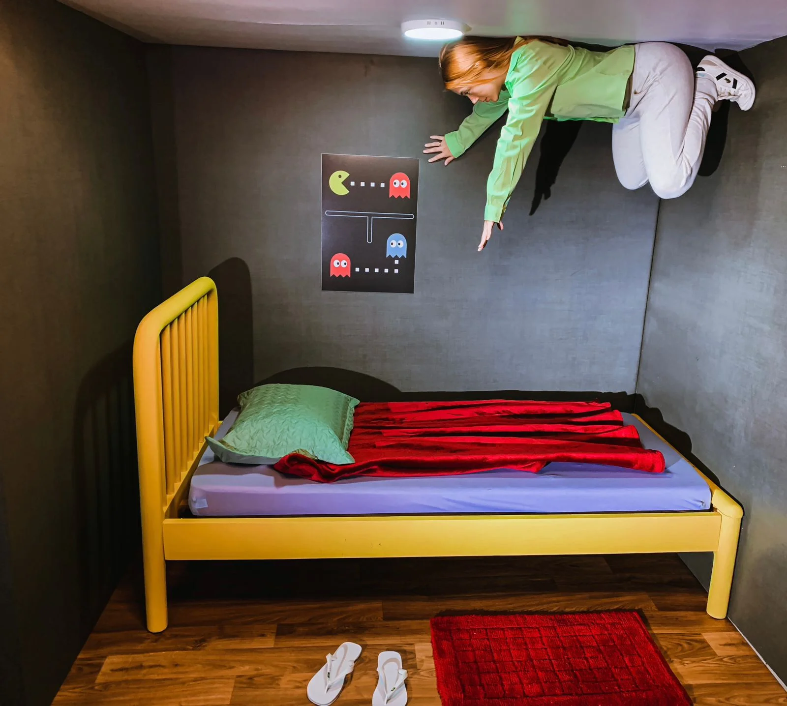 Pessoa flutuando sobre uma cama amarela em um quarto gamer, diante de um pôster de Pac-Man