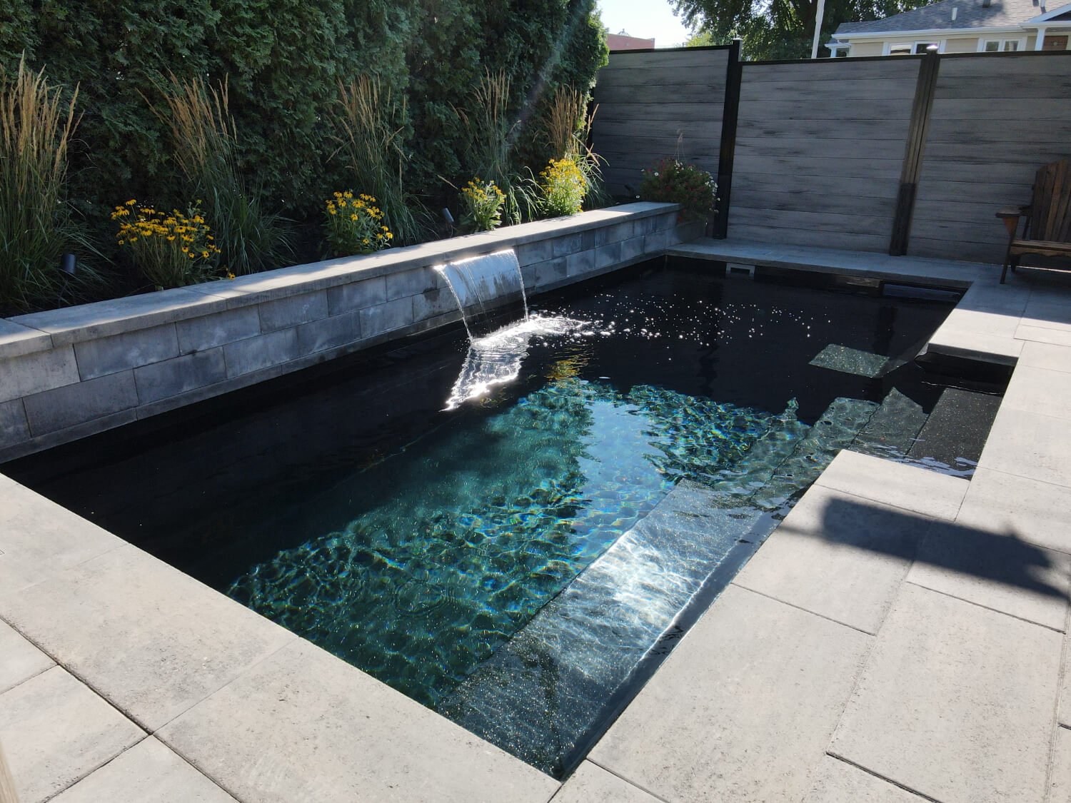 Black fiberglass inground pool with water feature and landscaping