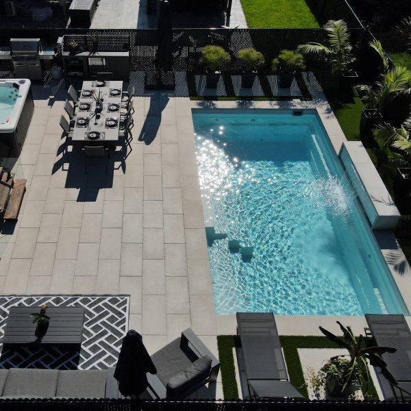 Overhead view of a completed pool installation with turquoise water, gray concrete deck, and green lawn