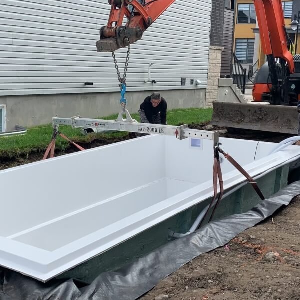 Rectangular pool with beige paver deck, white lounge chairs and green shrubs