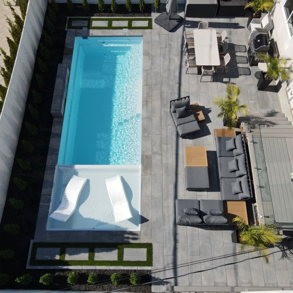 Aerial view of a modern backyard with turquoise pool, gray patio, and landscaping